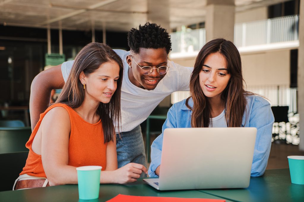 three happy students looking at a laptop 