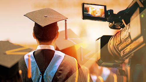 Image of a student wearing a cap and gown with a video camera recording the event.